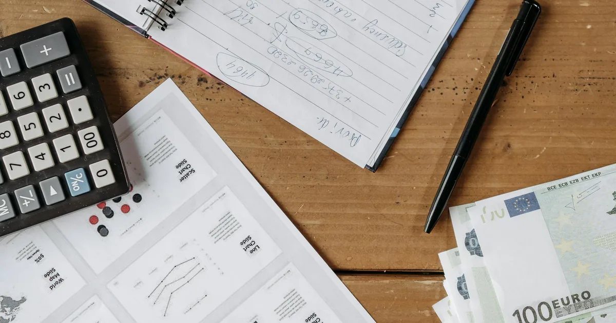 Overhead view of financial workspace with notebook, calculator, charts, and dollar bills — Shopify order accounting flow in QuickBooks Online