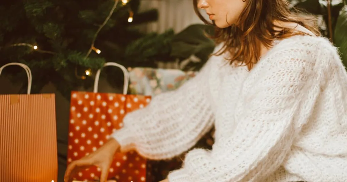 Woman in a knitted sweater wrapping Christmas gifts — Shopify merchant December 2025 holiday playbook