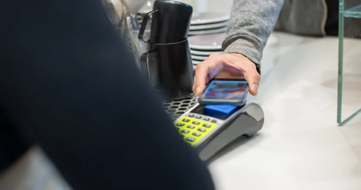 Customer making contactless smartphone payment at café counter — Shopify tips tracked as dedicated income in QuickBooks Online
